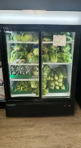 A glass-door fridge packed with lettuce, romaine hearts and other leafy greens in green crates