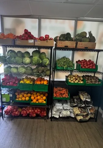 Two tall wire shelving units filled with cabbages, tomatoes, oranges, peppers, pineapples, green beans, carrots and bagged onions