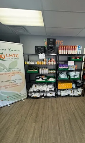 Stocked shelves beside the LHTC Food Bank roll-up banner, which reads “Welcome / Bienvenue” and “Let us end food insecurity together”
